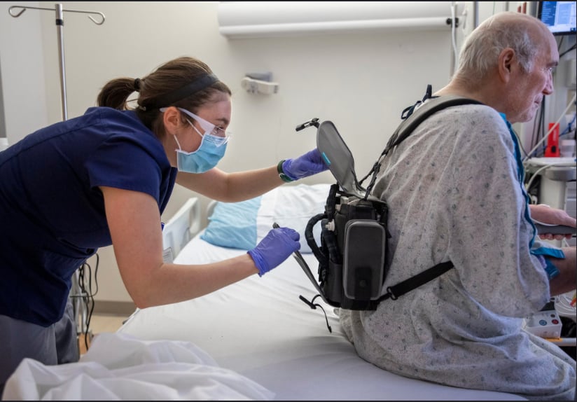 Brittany Rohrer, OT, helps patient Richard Hugginswith his Evaheart2 LVAD controller and power unit backpack before a a rehabilitation session.