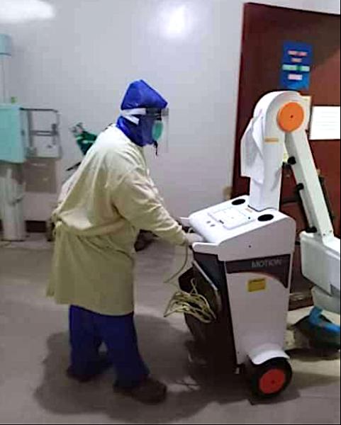 A radiology technologist using a rain coat and home-made face shield personal protective equipment (PPE) due to a severe shortage of PPE at Sen. Gerardo M. Roxas Memorial District Hospital in Iloilo City, Philippine. The techs used spoiled X-ray film with the emulsion stripped off, foam packing material, elastic and a glue gun to make their own face shields. Photo by Dodge Moises, radiology technologist.